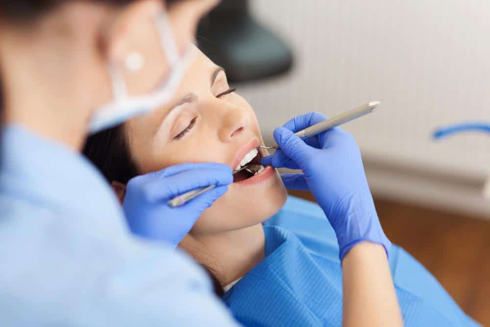 dentist cleaning and inspecting woman's teeth