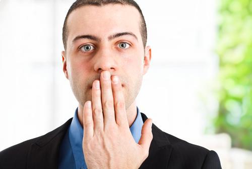 man holding his hand over his mouth to prevent his bad breath from spreading
