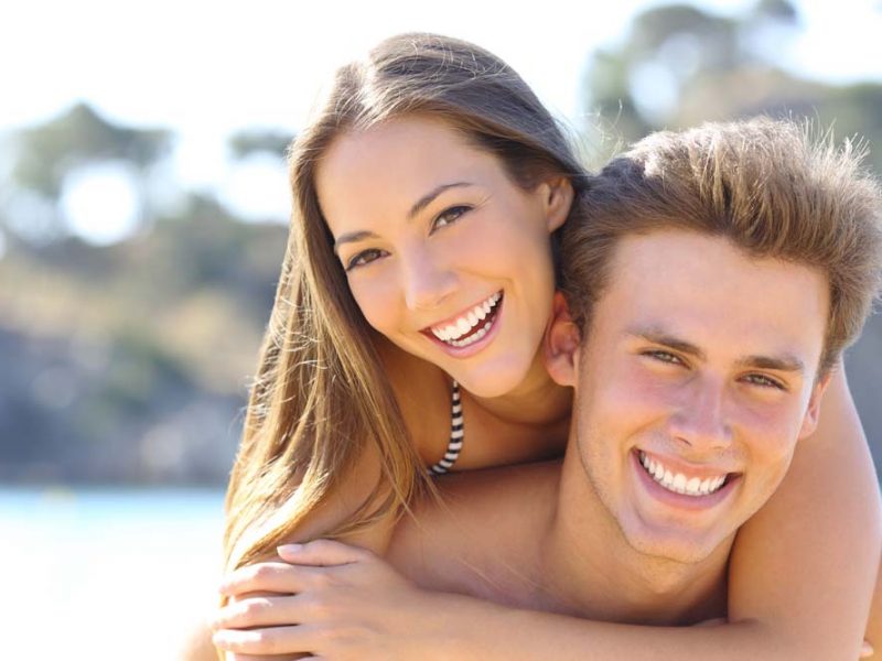 Happy couple with perfect smile and white teeth posing on the beach looking at camera
