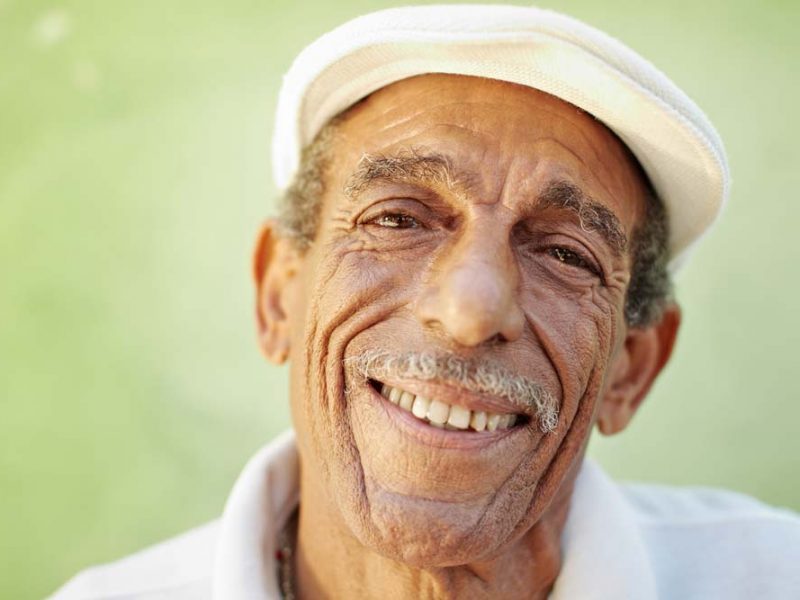 portrait of senior hispanic man with white hat looking at camera against green wall and smiling. Horizontal shape, copy space