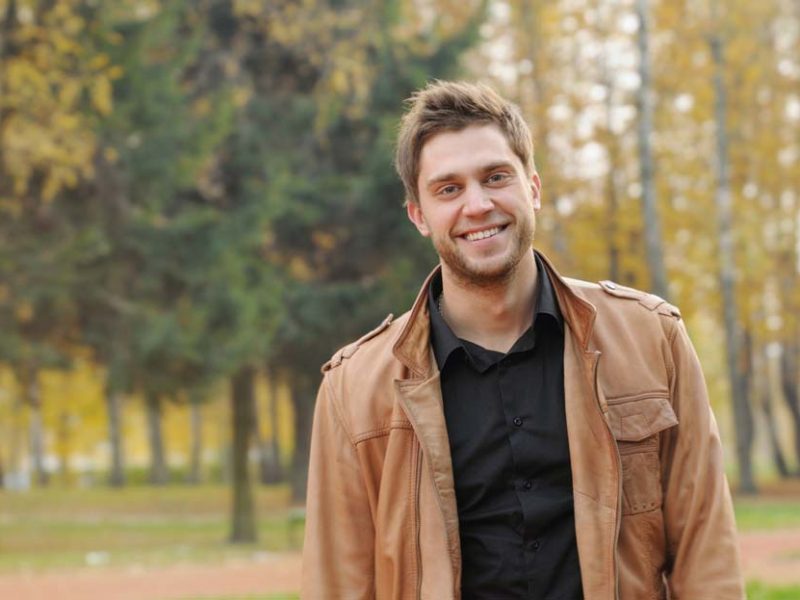 portrait of attractive happy smiling stylish young man in autumn park, outdoors background